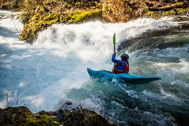 Person kayaking through a rapid river with rapids and rocks.